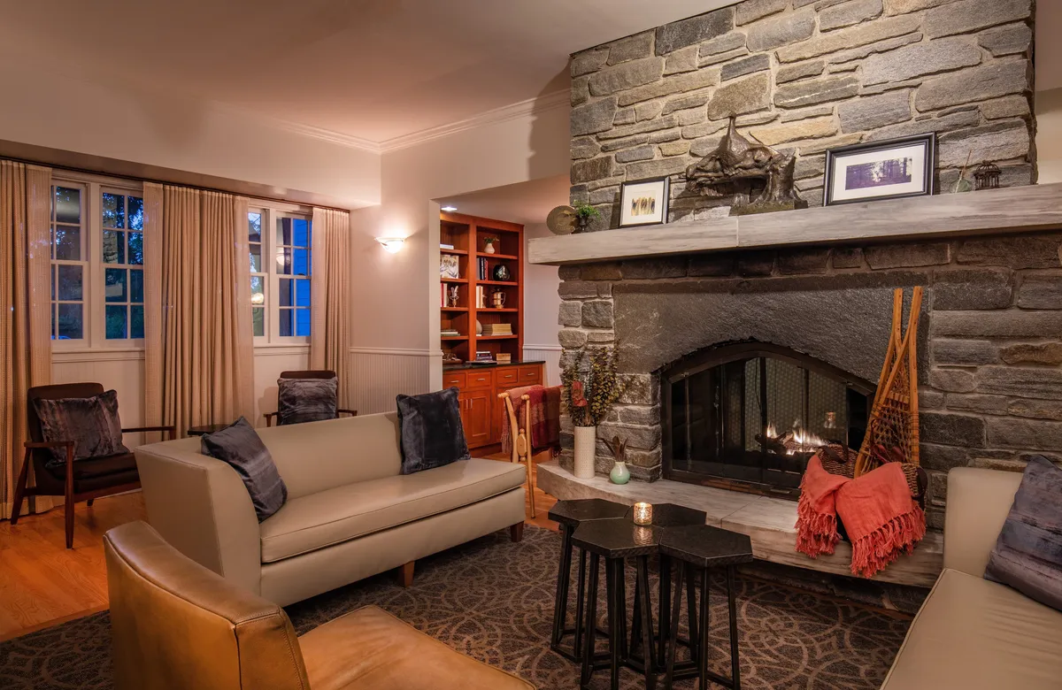 A cozy lounge room featuring a grand stone fireplace, plush seating, and a well-stocked bookshelf, evoking warmth and comfort. The space is perfect for quiet moments, reading, or intimate gatherings, reflecting the sanctuary-like aspect of the resort.