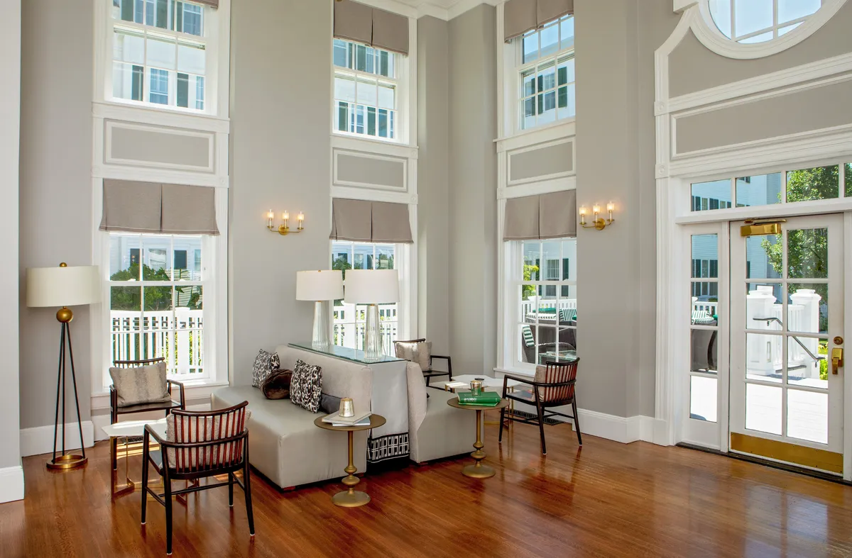 An elegant guest room interior featuring large windows that fill the space with natural light, a stylish seating arrangement, sophisticated light fixtures, and a decorative coffee table. The ambiance is both comfortable and refined, hinting at a space tailored for relaxation or planning a day’s adventure.