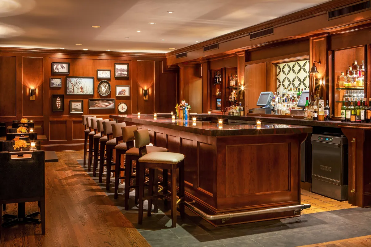 A welcoming interior bar and lounge area, with a stylish bar counter, plush stools, art-adorned walls, and shelves stocked with bottles. The space exudes a cozy, social vibe, perfect for gatherings and unwinding after activities.